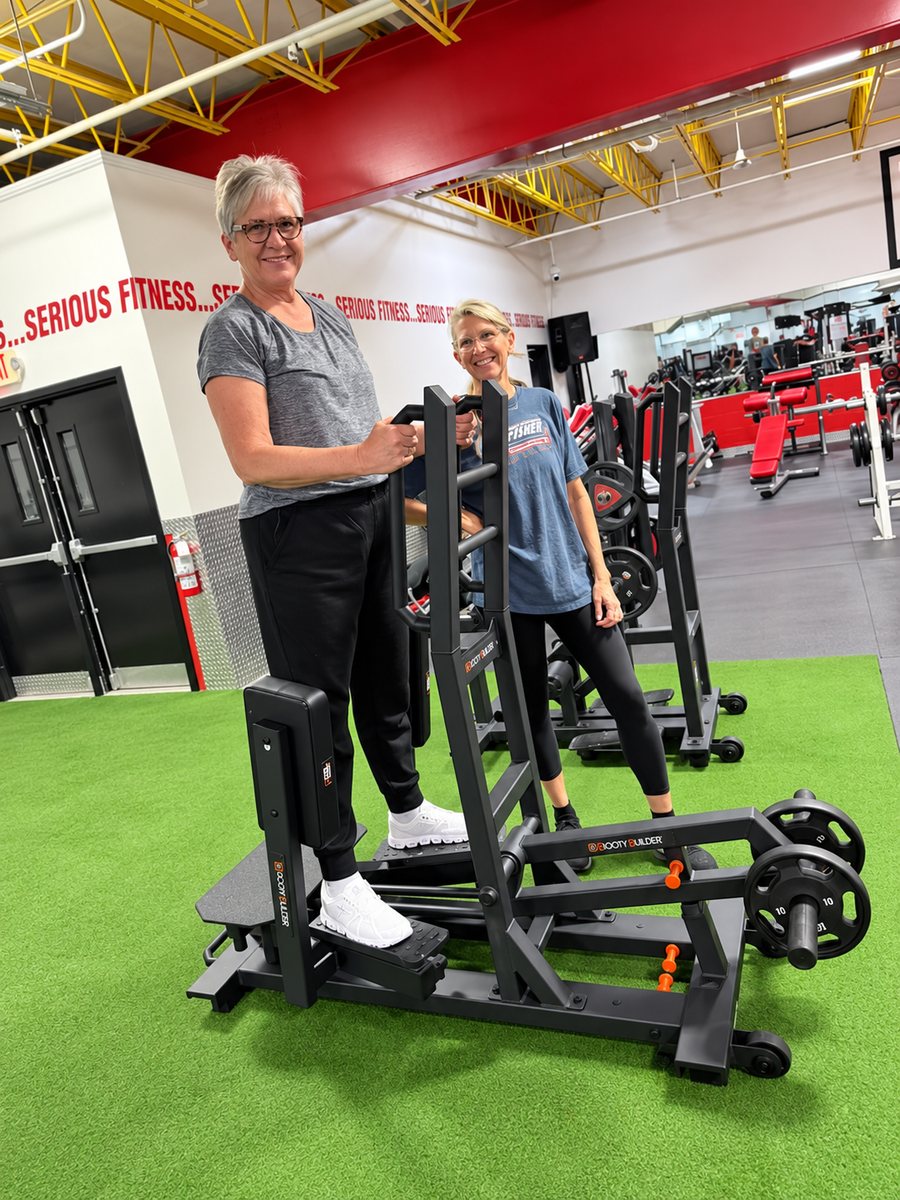 Two women laughing while training on a Booty Builder machine